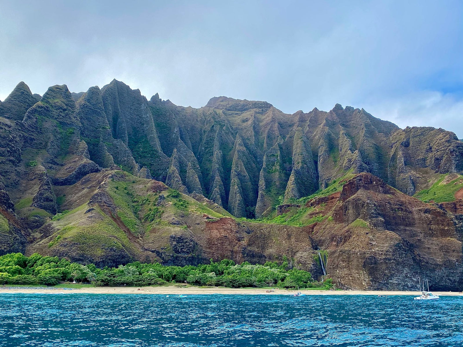 Na Pali Coast, Hawaii: towering green cliffs, beach, waterfall, blue ocean. An RV rental could explore similar wonders elsewhere.