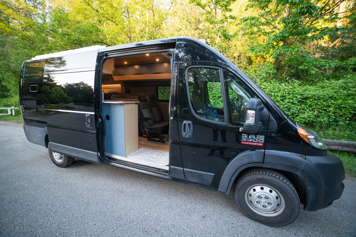 Sleek black RAM ProMaster camper van for rv rental. Open side reveals its custom wood interior with bed & seating. — photo 4