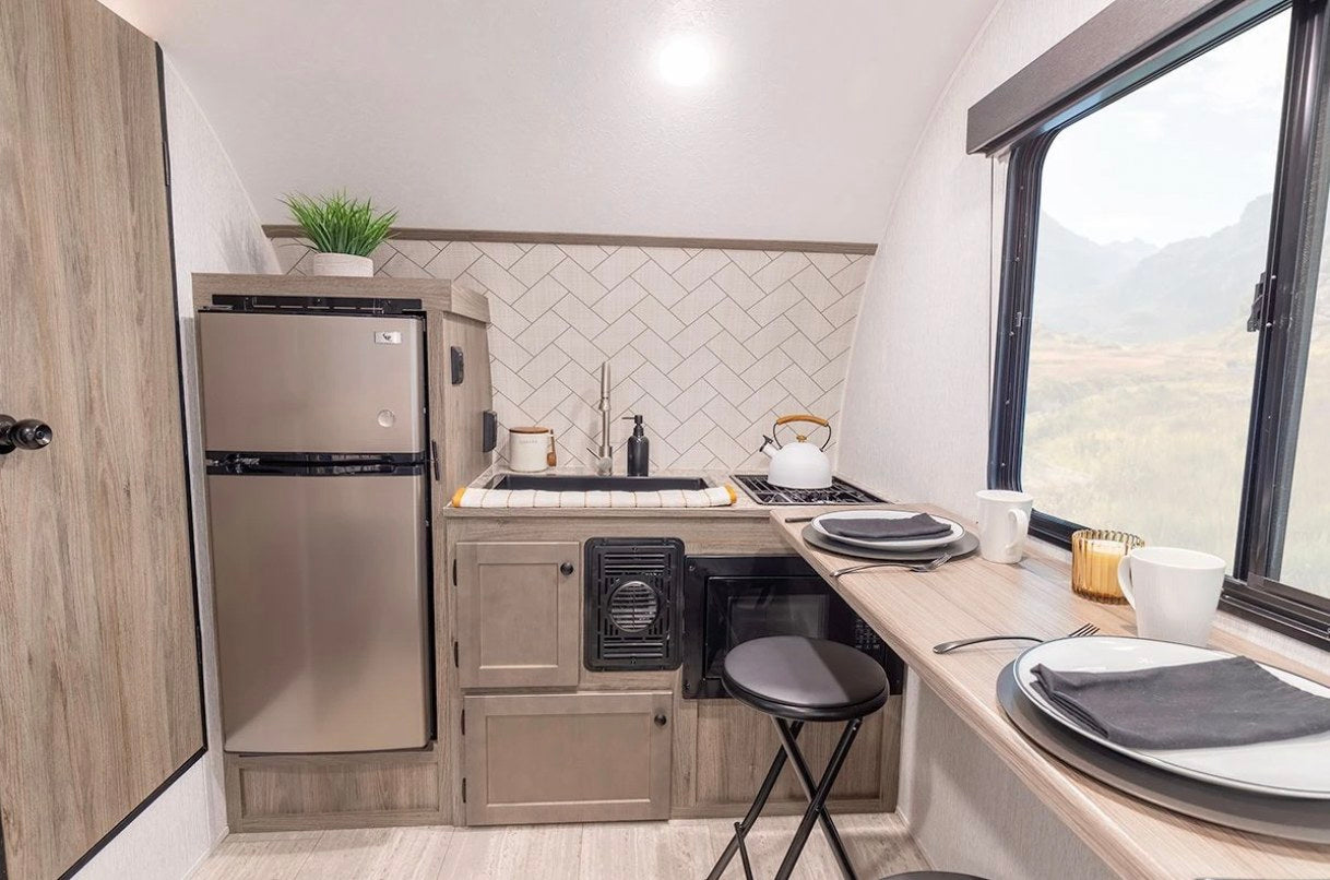 Experience this modern RV rental's kitchen. It features a fridge, sink, cooktop, microwave, and bar dining with a mountain view.
