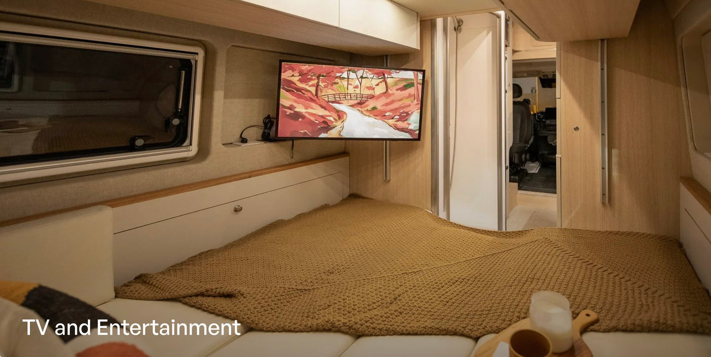 This cozy rv rental bedroom features a wall-mounted TV for entertainment above a comfortable bed and window.
