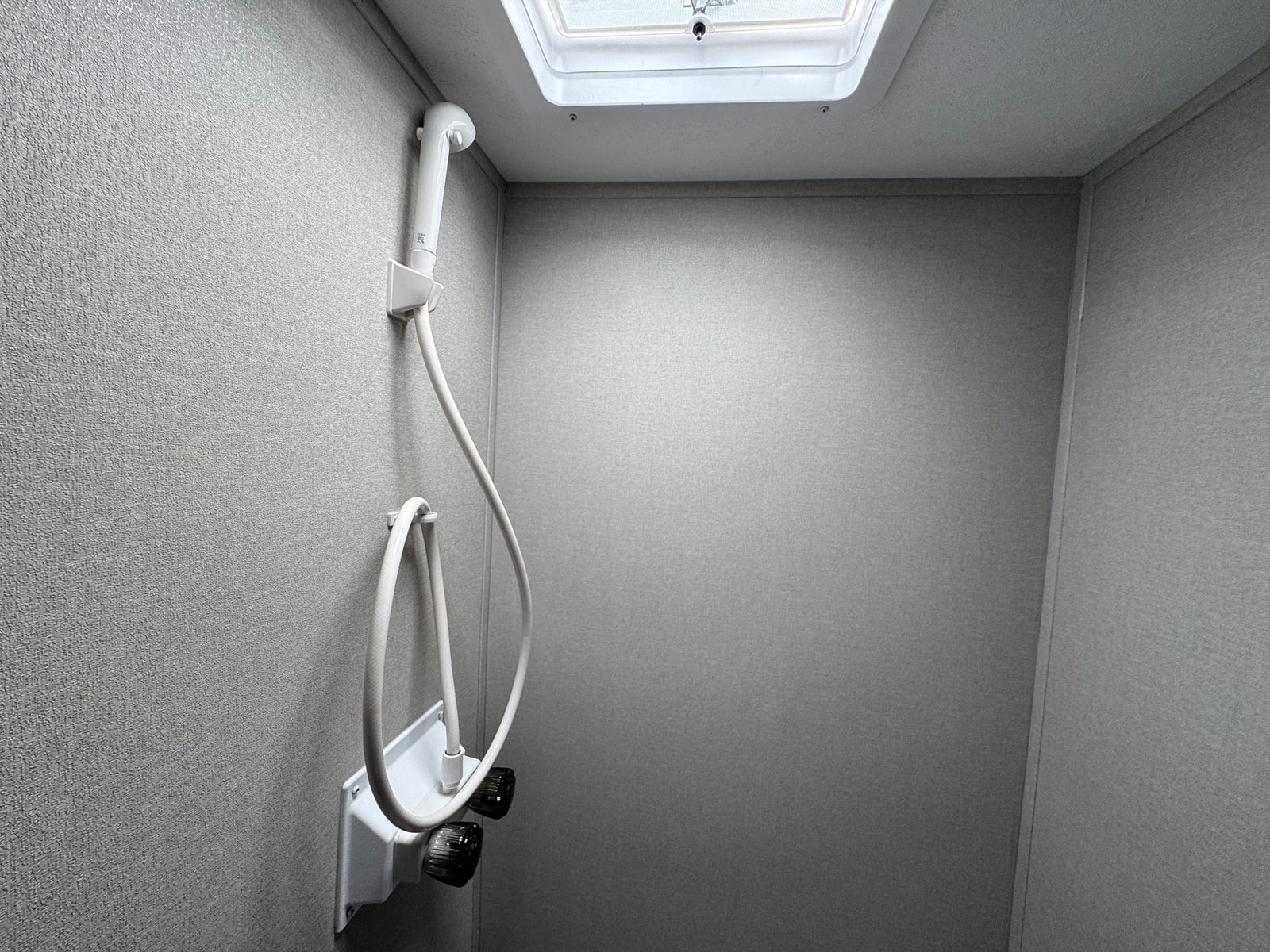 Inside an RV rental: a modern, light-grey shower stall with a handheld shower and accessible controls. Features a ceiling vent.