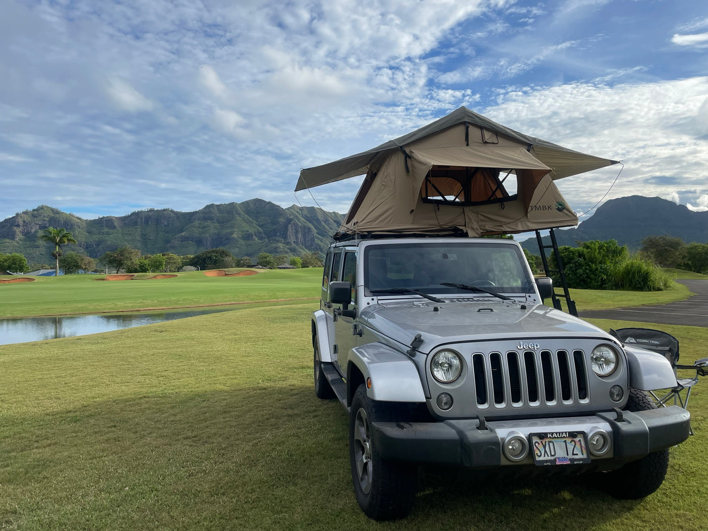 Silver Jeep with rooftop tent on Kauai's scenic golf course. An RV rental alternative for mountain adventures.