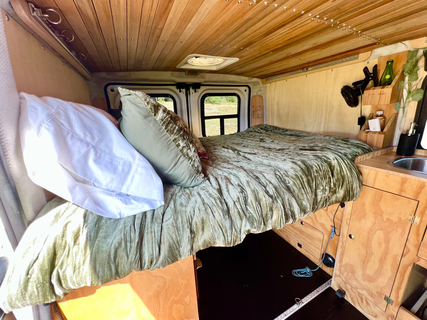 Cozy rv rental interior featuring a comfy bed with green bedding, wooden paneling, and a compact sink area.