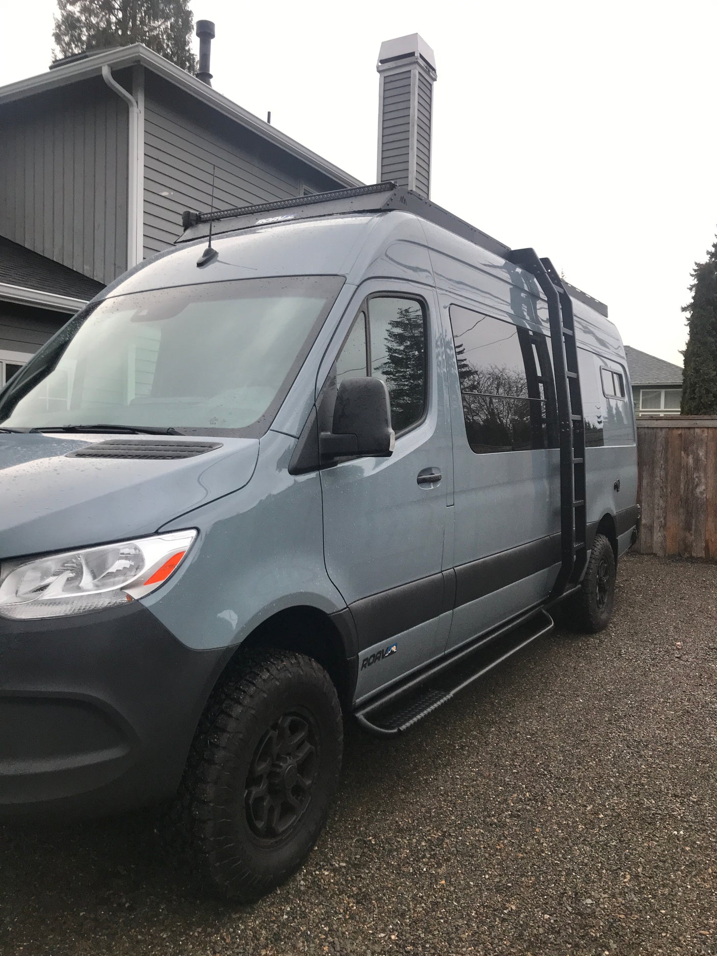 Gray custom-built Mercedes-Benz Sprinter camper van, equipped for adventure, perfect for an RV rental experience, parked on gravel.