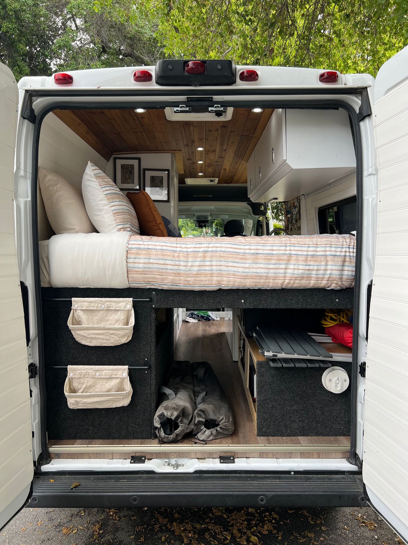 Cozy camper van interior viewed from rear: bed with striped bedding, under-bed storage, wood ceiling. Great for RV rental.