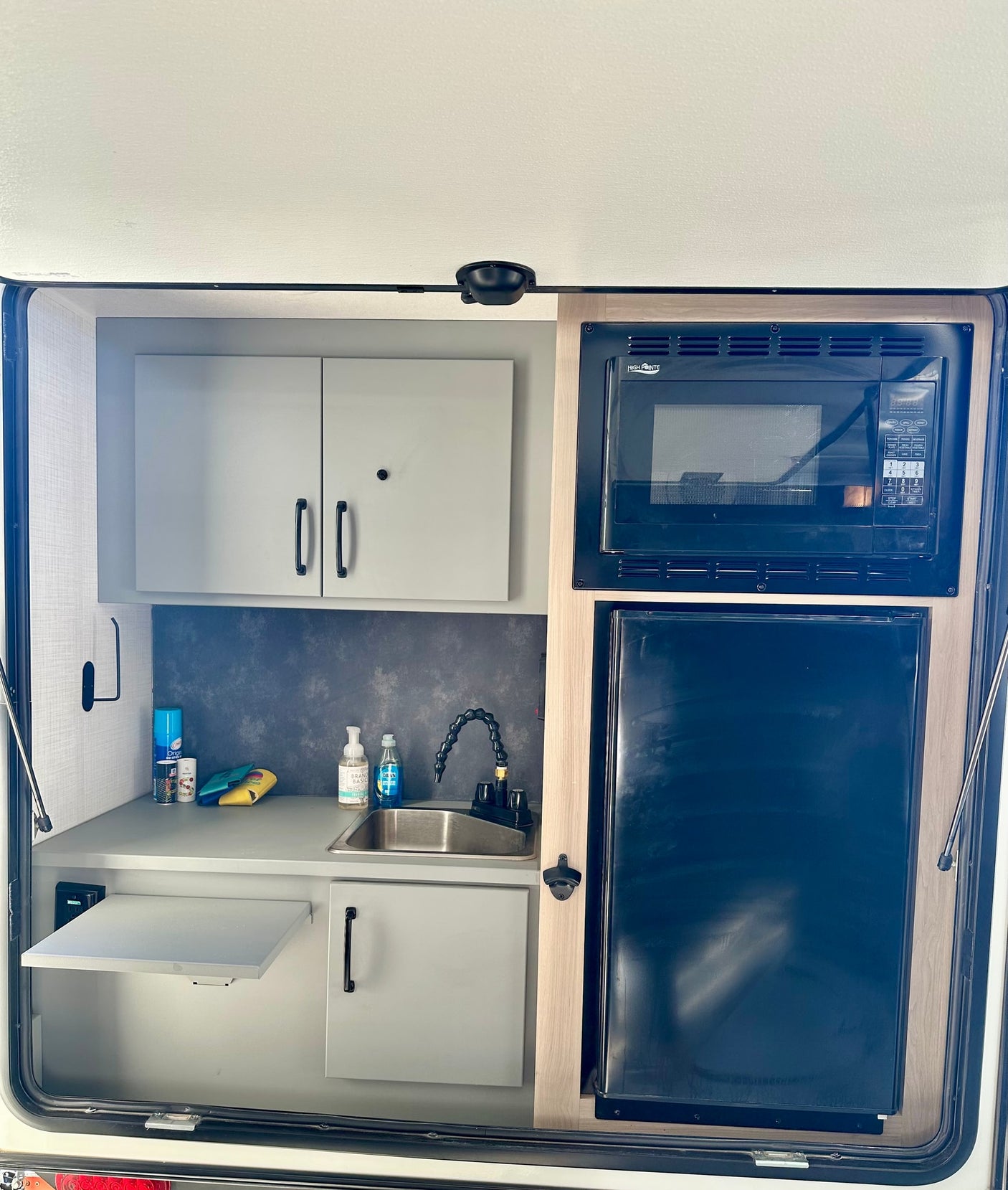 Compact RV rental outdoor kitchen with sink, microwave, fridge, pull-out shelf, and storage for convenient camping.