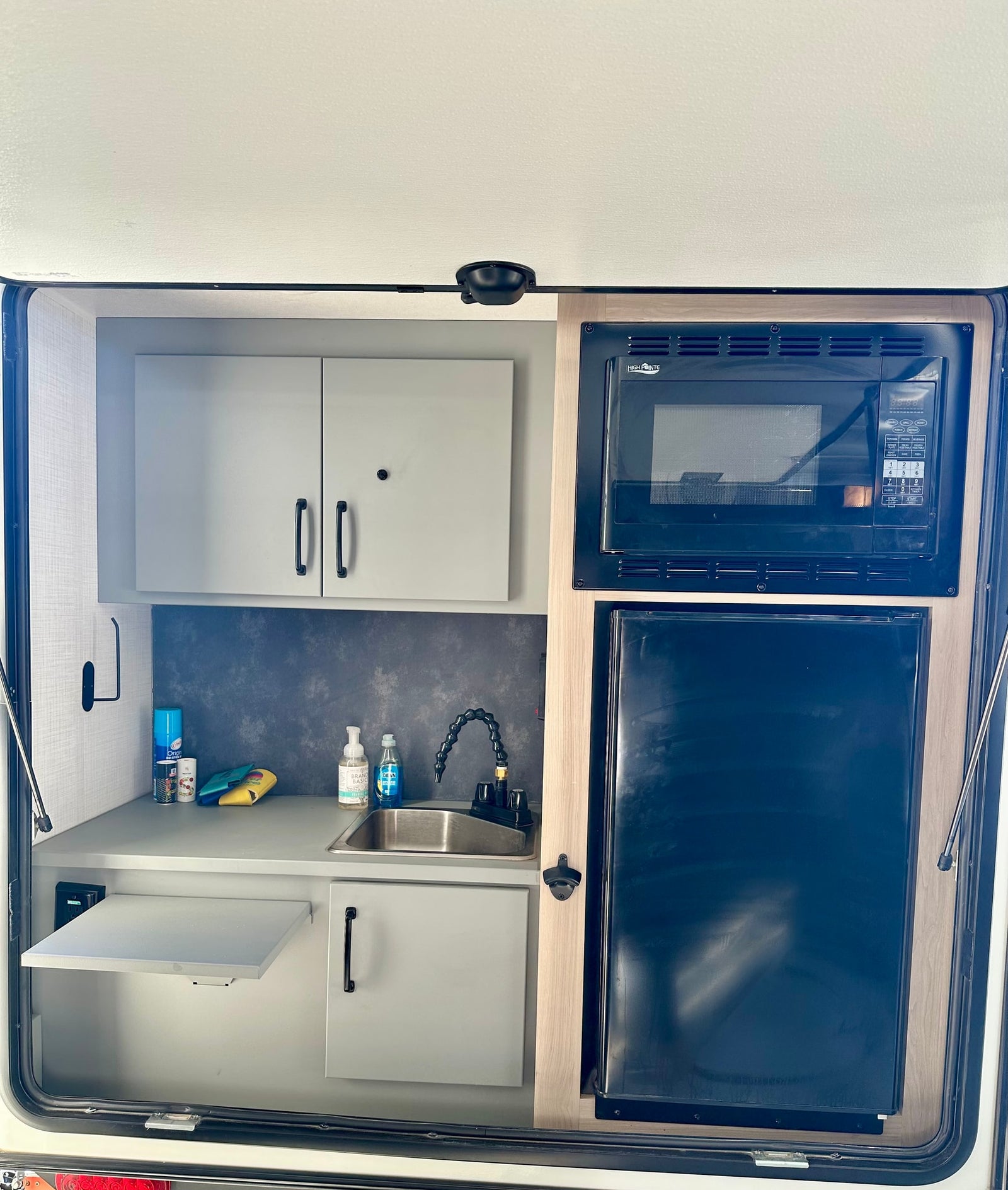 Compact RV rental outdoor kitchen with sink, microwave, fridge, pull-out shelf, and storage for convenient camping.