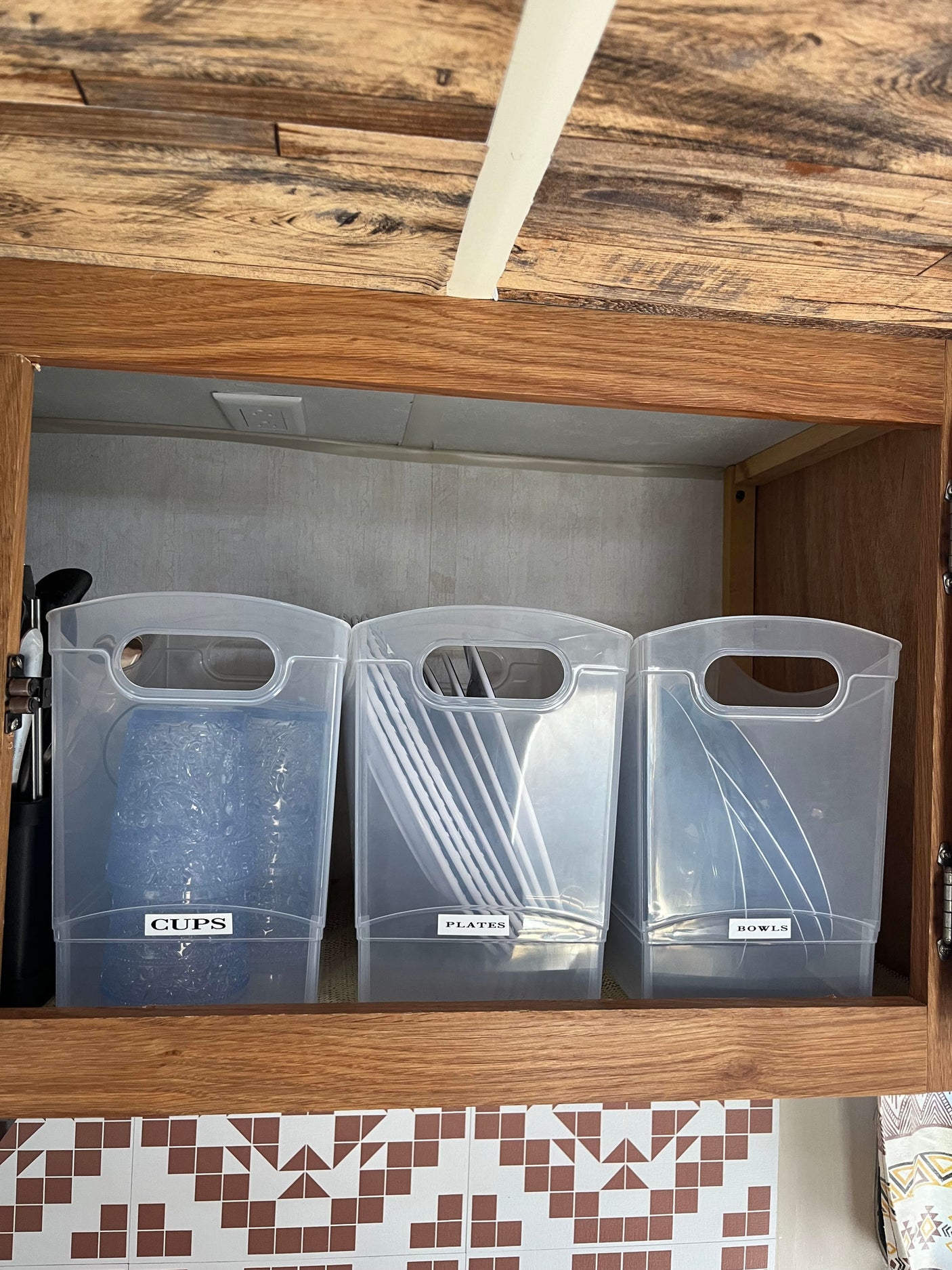 Efficient RV rental storage: clear bins keep cups, plates, & bowls organized in this kitchen cabinet.