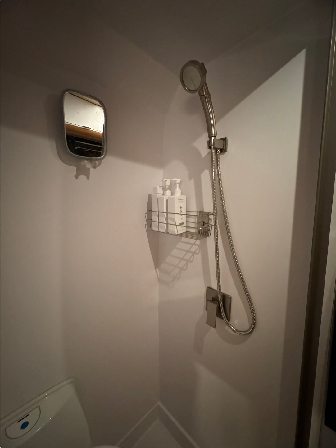 Compact RV rental bathroom: White shower stall, mounted mirror, shower head, toiletries, and toilet below. Efficient space.