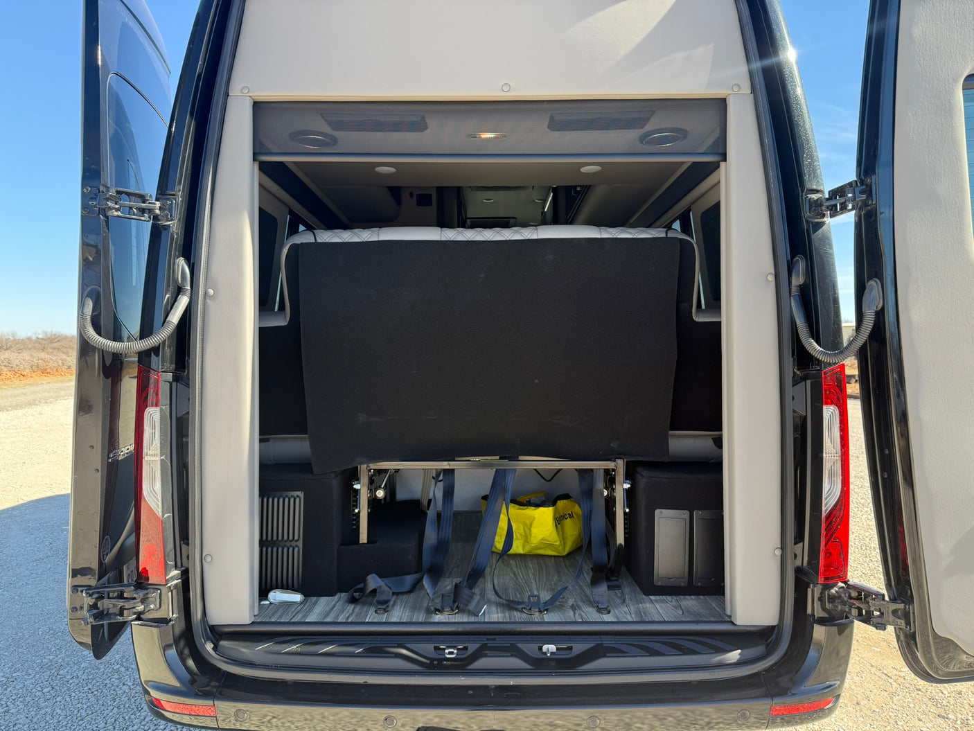 Rear view of an RV rental camper van with open doors, showcasing its versatile interior bed and storage area.