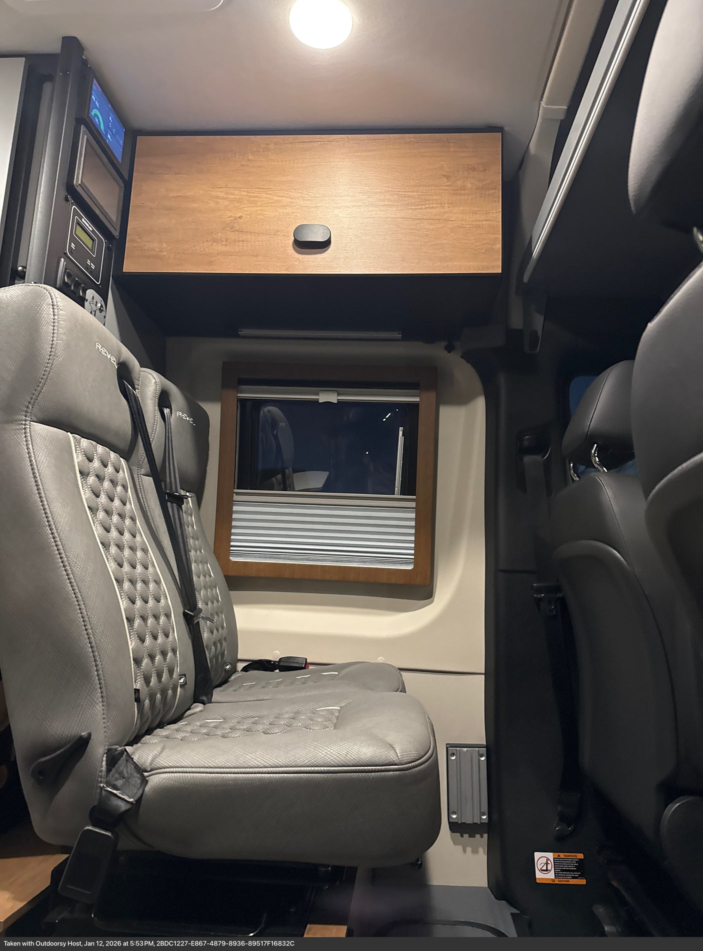 Winnebago Revel RV rental interior: gray quilted seats, wood cabinet, window with blind, and control panel. Ready for adventure.