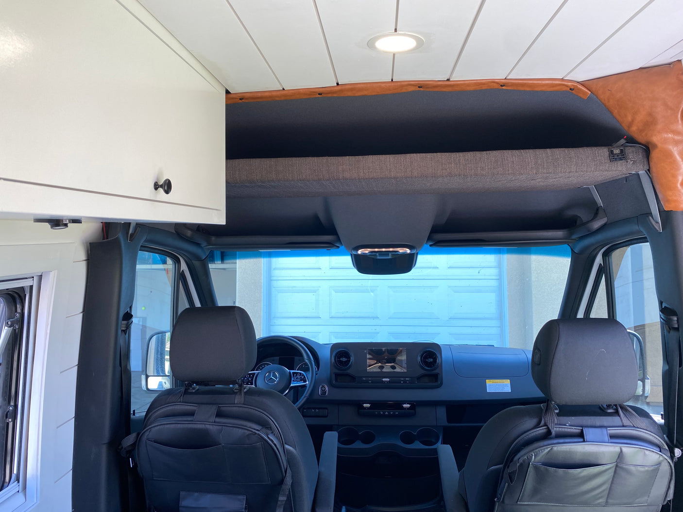 Inside an RV rental: Looking forward from the custom living space to the driver's cabin with overhead storage.