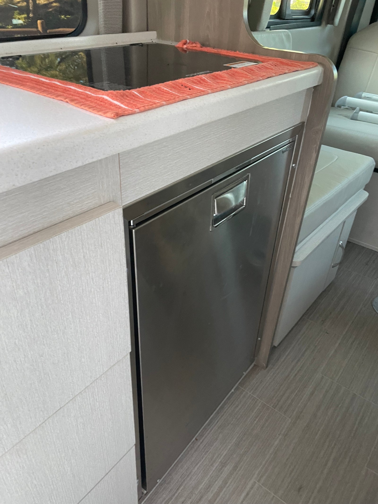 Modern RV rental kitchen with cooktop, stainless fridge, and light wood cabinetry for compact living.