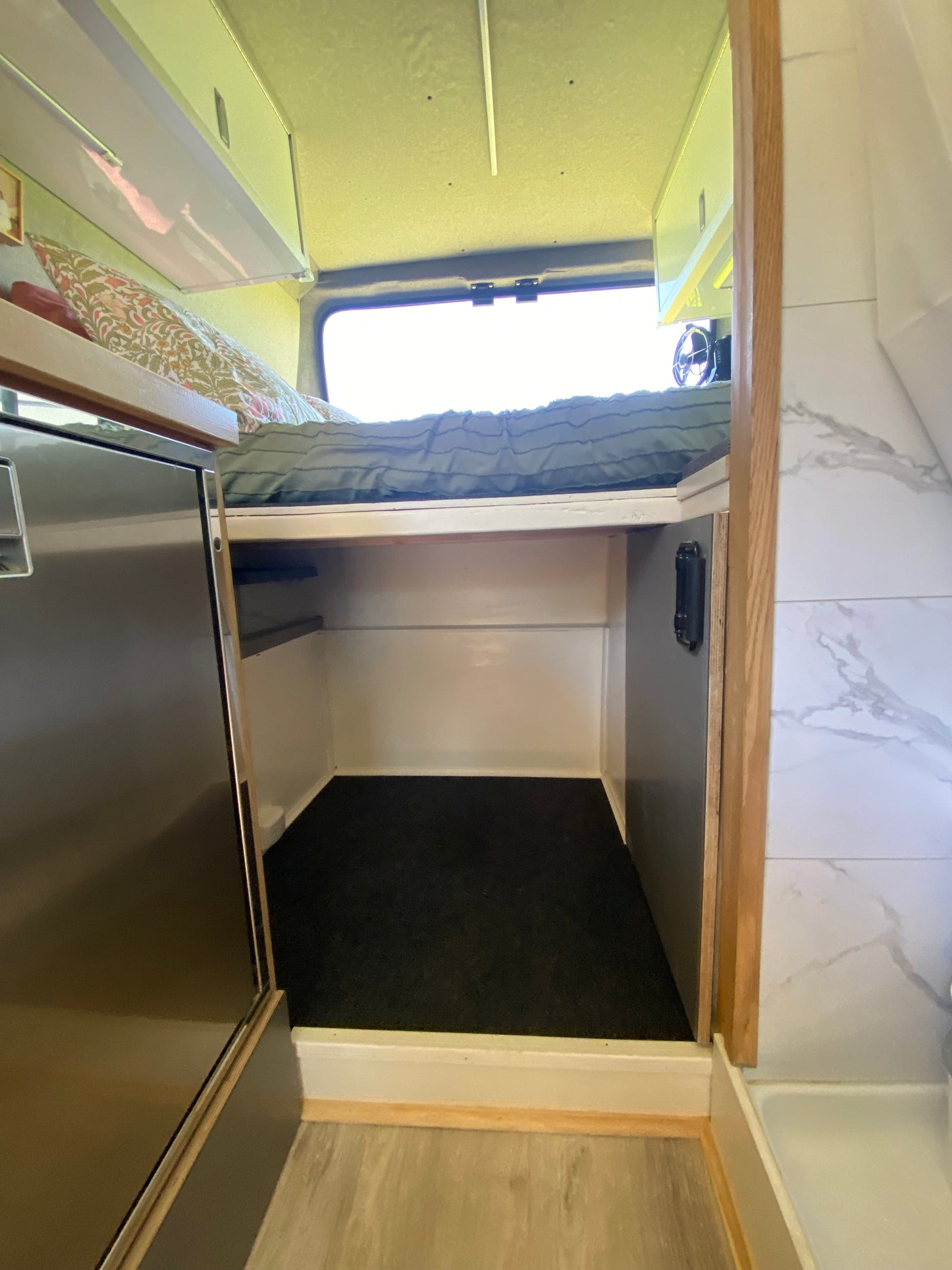 Cozy RV rental interior with a bed, under-bed storage, fridge, and stylish tiled wall.