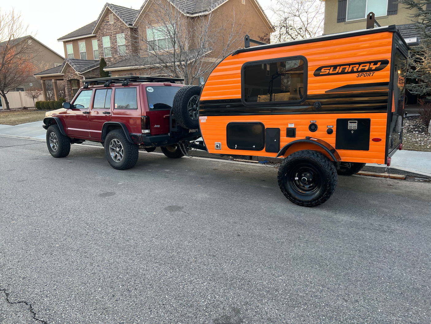 Red Jeep Cherokee towing a vibrant orange Sunray Sport RV rental on a street, ready for adventure.