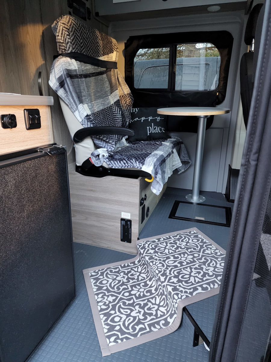 Inside a cozy RV rental: a comfy patterned chair with blankets, a small table, and a fridge on a textured floor.