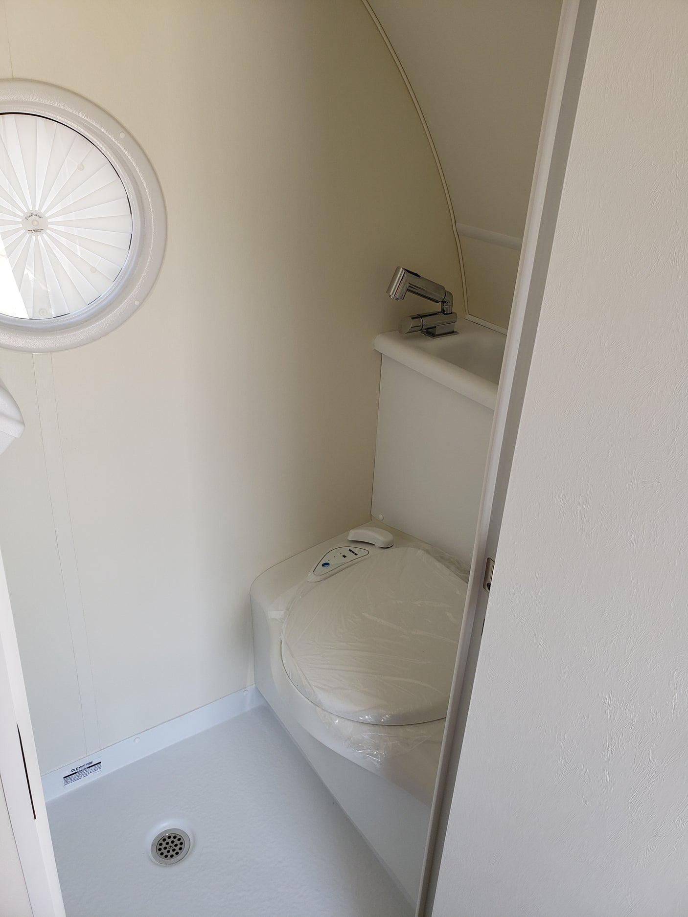 RV rental's small bathroom with toilet, sink, shower drain, and a pleated window shade.