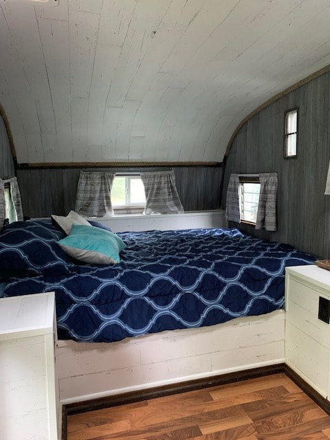 Cozy RV rental bedroom with white plank walls, blue patterned bedding, and wood floors. Perfect for mobile living.