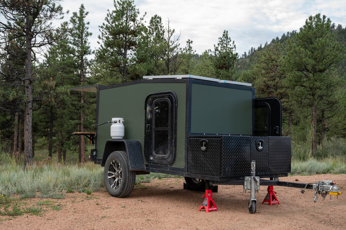 This rugged green camper is ready for your next **RV rental** adventure. Features propane, solar, and storage, set among pine trees.