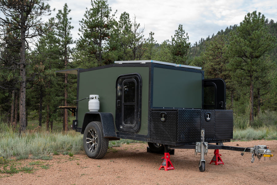 This rugged green camper is ready for your next **RV rental** adventure. Features propane, solar, and storage, set among pine trees.