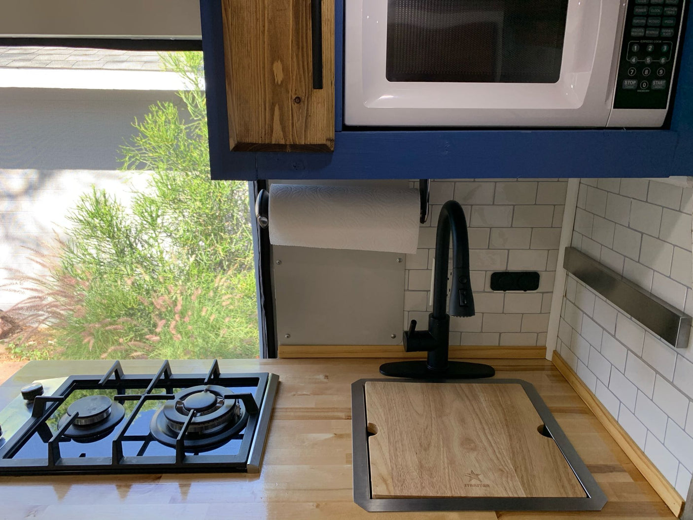 RV rental kitchen: Compact design with a stovetop, sink, microwave, and bright window view.