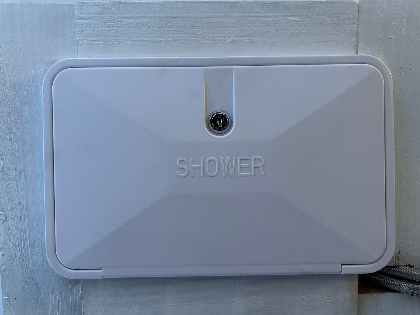 White rectangular exterior shower panel with a keyhole, embossed "SHOWER," for an RV rental.