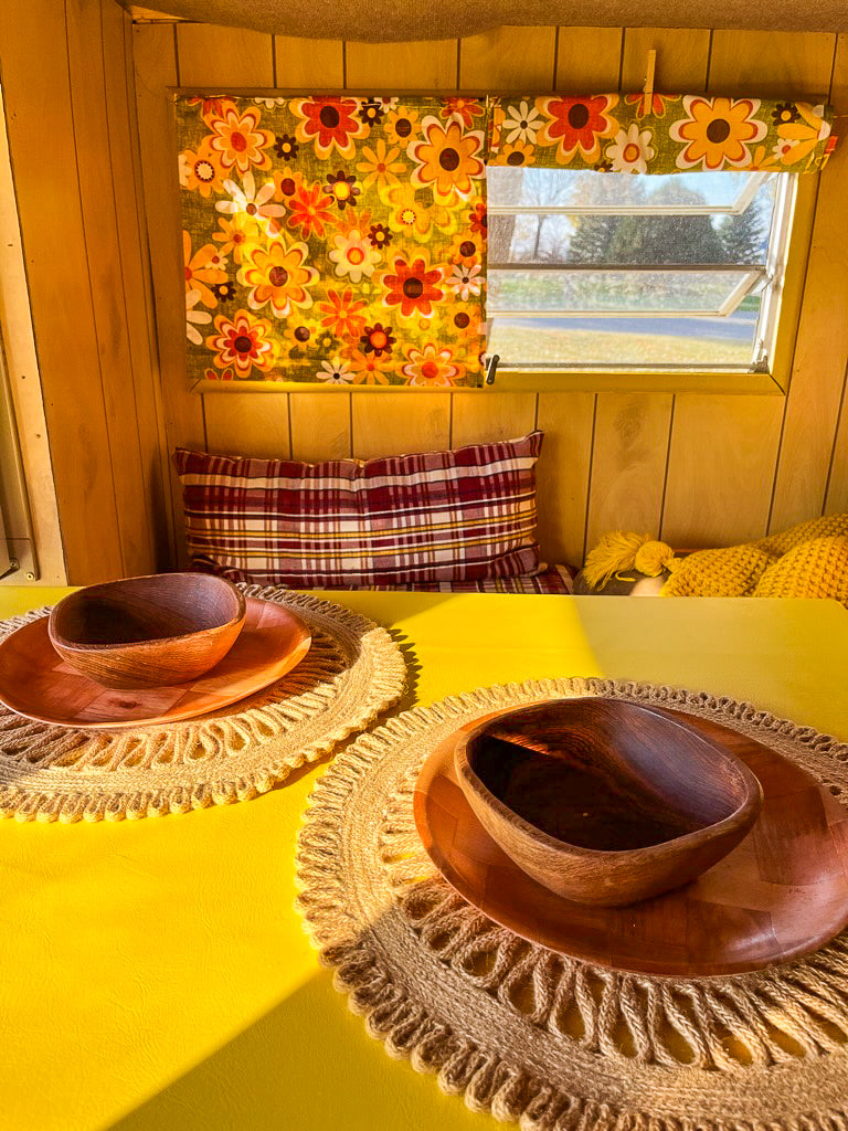 Our charming rv rental offers sunlit dining. Vintage floral curtains, wood paneling, and wooden dishes.