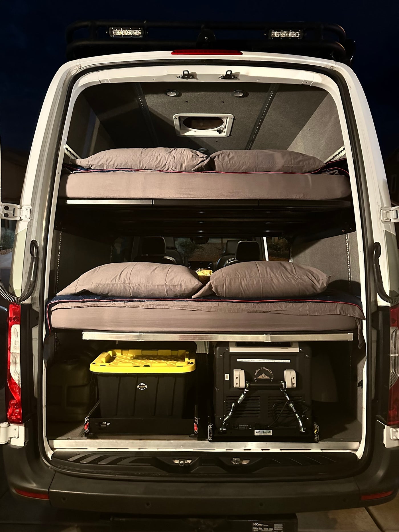 Inside an RV rental camper van: stacked bunk beds with bedding, storage bins, and a portable fridge/freezer for adventure. — photo 17