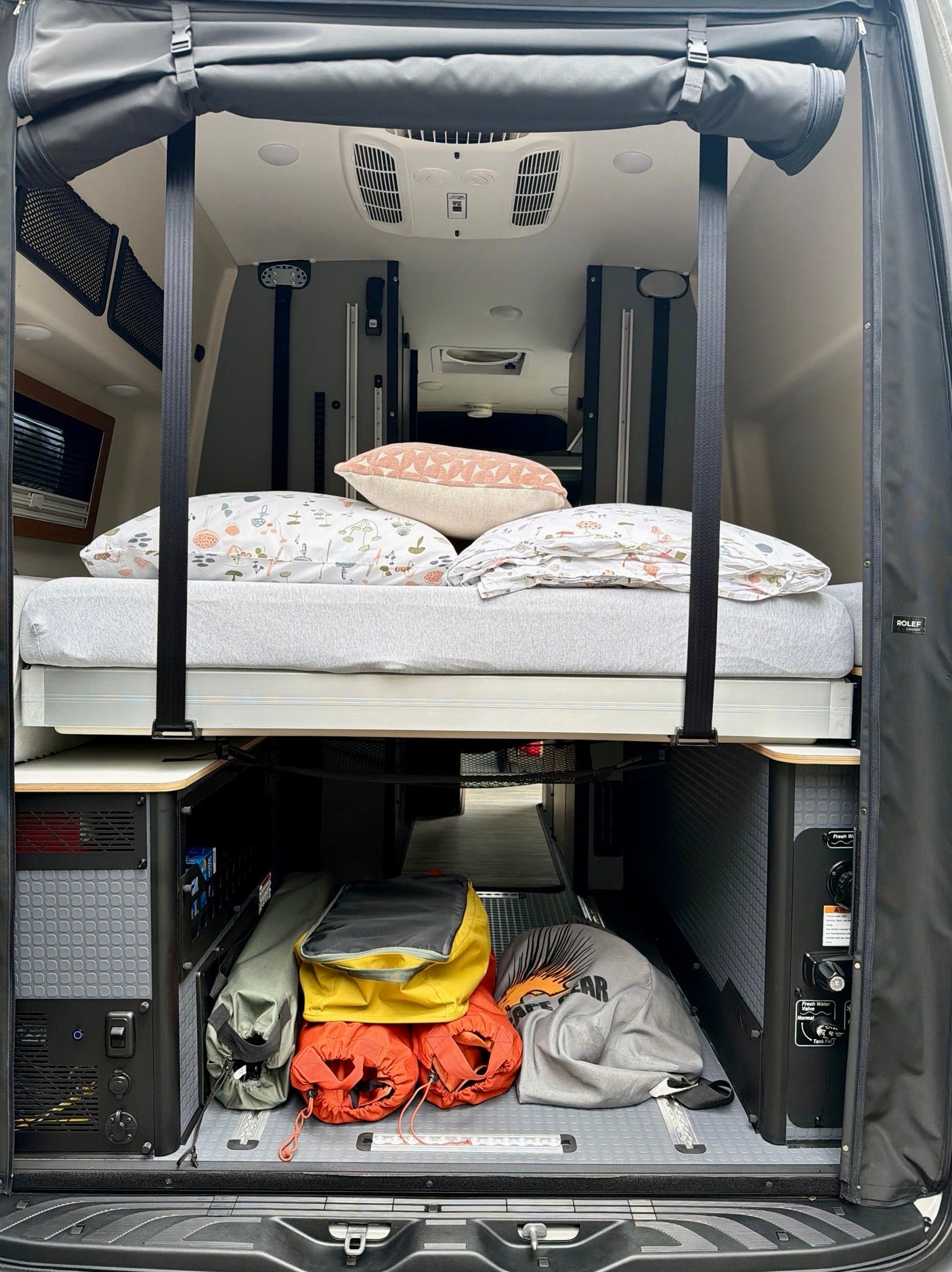 RV rental interior: elevated bed with cozy pillows, and smart storage for camping gear & utility access below. Rolef camper van.