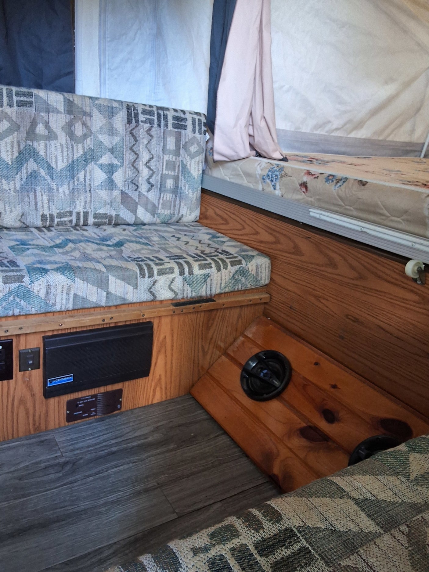 Inside an rv rental: patterned cushions, wood panels, gray flooring, and sleeping area. A compact camper interior.