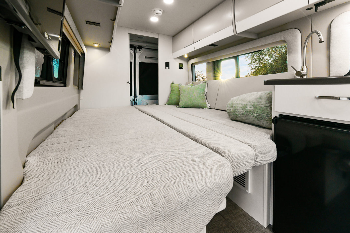 Spacious rv rental interior: comfy bed, mini-kitchen, and scenic window views through a large window.