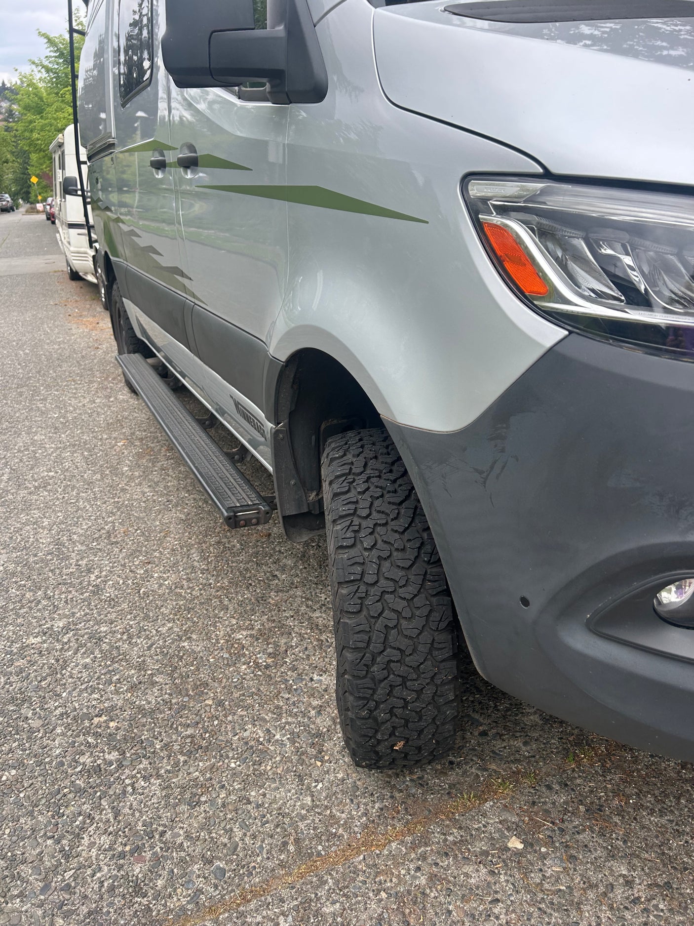 This silver rv rental van, equipped with rugged off-road tires and green graphics, looks ready for any adventure.