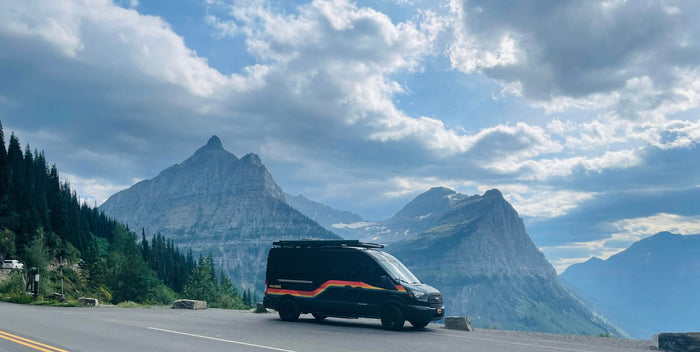 Experience majestic mountain views with this Vandalit RV rental van parked on a scenic road, surrounded by towering peaks and forests.