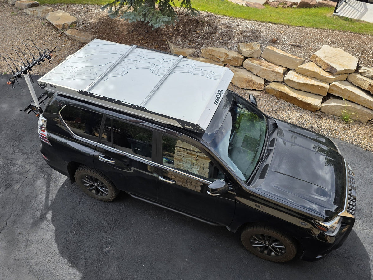 Overhead view of the closed Terrapod RTTx XL mounted on a black SUV, showing the full footprint of the white topo-print lid rack and the low-profile hard shell from above — photo 7