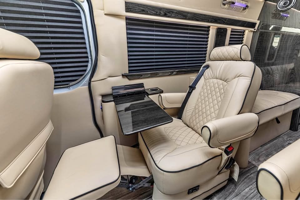 is parked on an asphalt driveway with trees.|Spacious RV rental interior featuring opposing cream leather seats