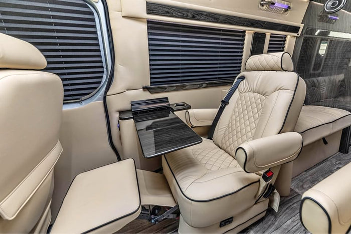 is parked on an asphalt driveway with trees.|Spacious RV rental interior featuring opposing cream leather seats