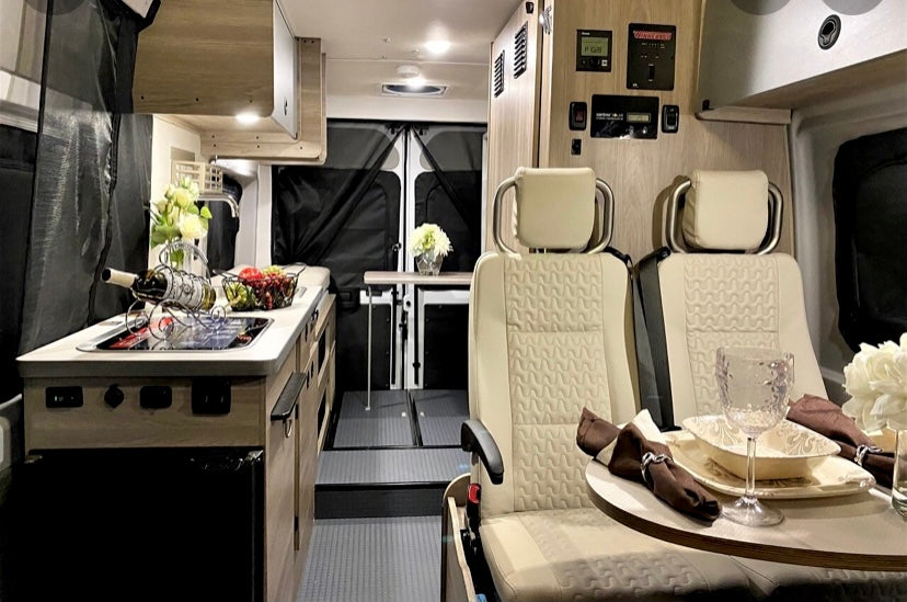 This inviting RV rental interior features a compact kitchen, comfortable dining area with swivel seats, and controls, perfect for travel adventures.