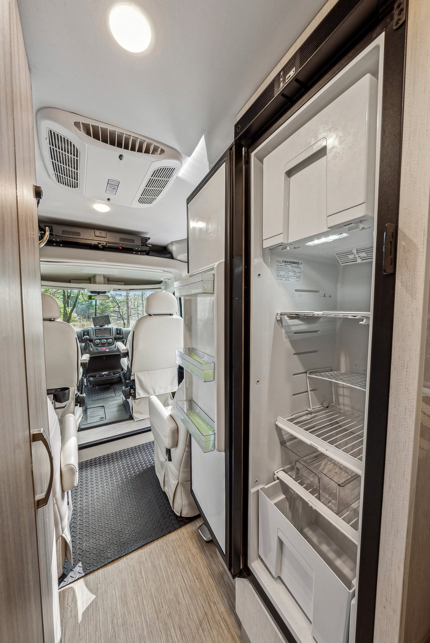 Explore this rv rental's organized interior. Features an open refrigerator, comfortable swivel seats, and an AC unit for comfort.