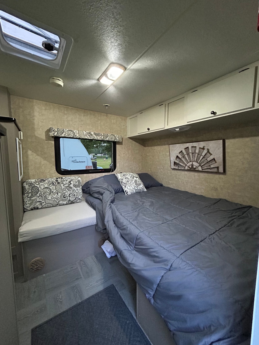 Inviting RV rental bedroom with a comfy bed, bench seating, overhead storage, and a scenic window view.