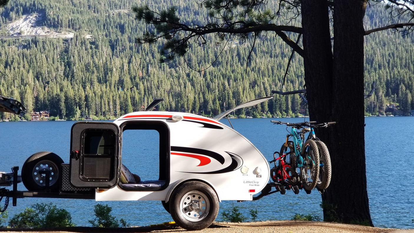 Little Guy teardrop rv rental with bikes by a scenic lake. An open door welcomes you to camping and adventure.