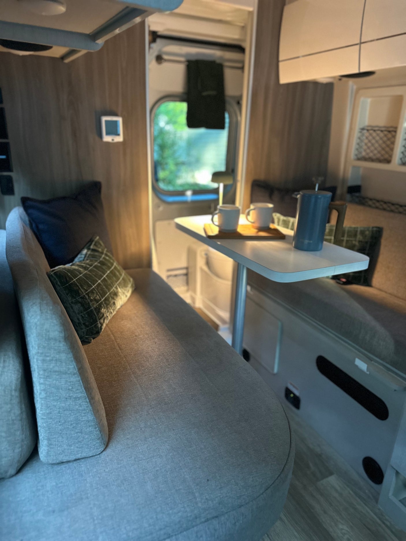 Cozy RV rental interior featuring a sofa with pillows, a dining table with coffee, and a view of nature for travel adventures.