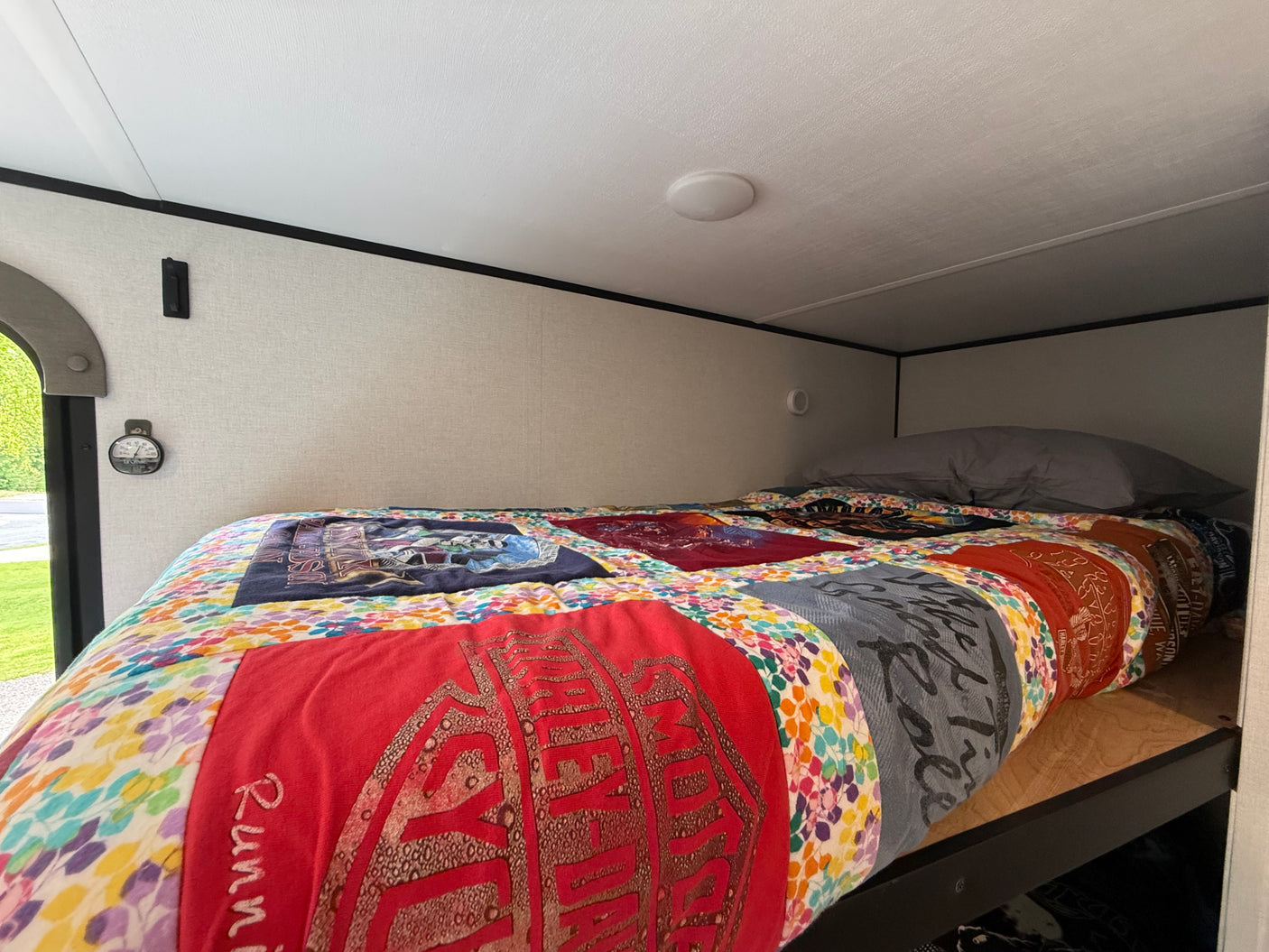 Colorful T-shirt quilt on a cozy bunk bed in an RV rental, with a ceiling light and outdoor window view.