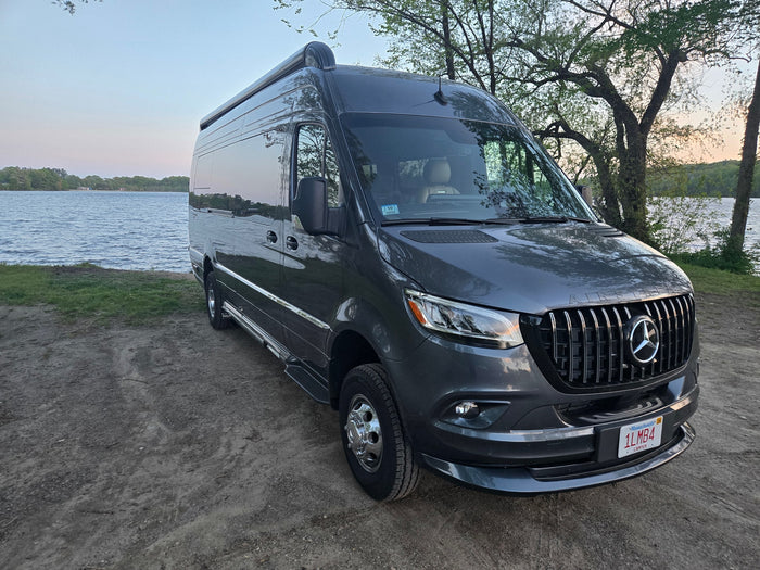 This sleek, grey Mercedes-Benz Sprinter rv rental is parked beside a tranquil lake, ready for a scenic camper van adventure.