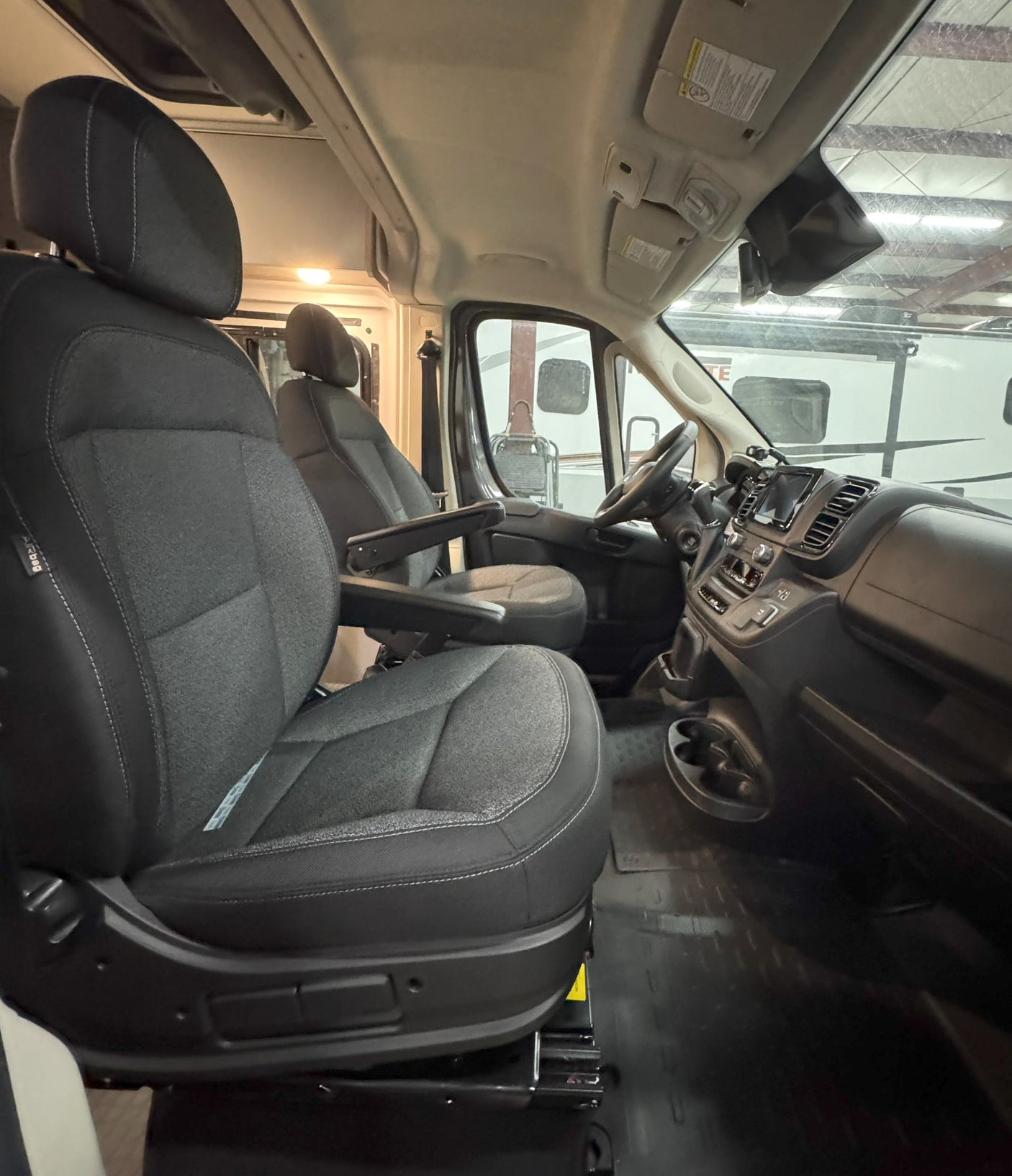 RV rental's front cabin: driver & passenger seats with armrests, a sleek dashboard. Clear view for your next road trip adventure.