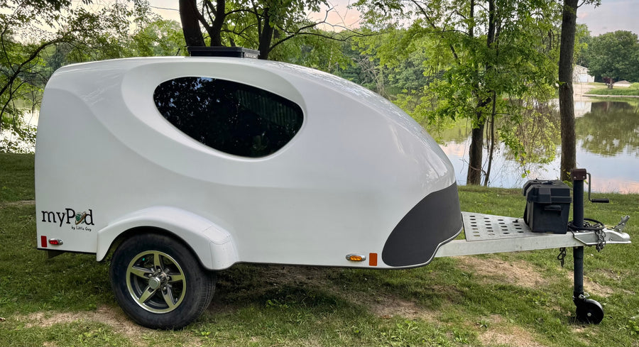 A compact myPod teardrop travel trailer, ideal for RV rental, parked by a scenic lake.