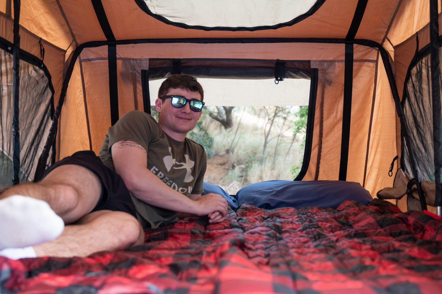 Relaxing inside a spacious **rooftop tent**, part of an **RV rental** adventure. Man smiles, enjoying the **outdoor** comfort.