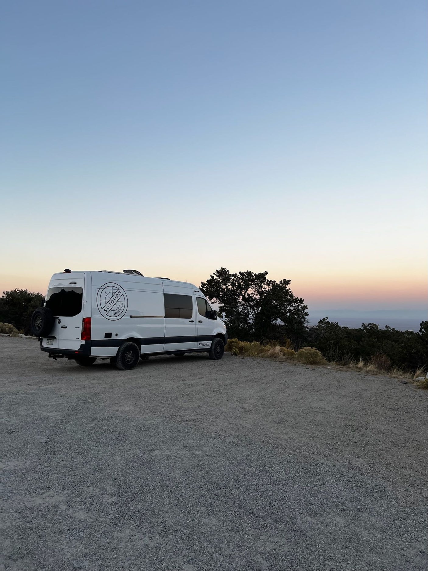 White Sojourn Sprinter **RV rental** parked at sunset, overlooking a scenic valley. Perfect for adventure travel.