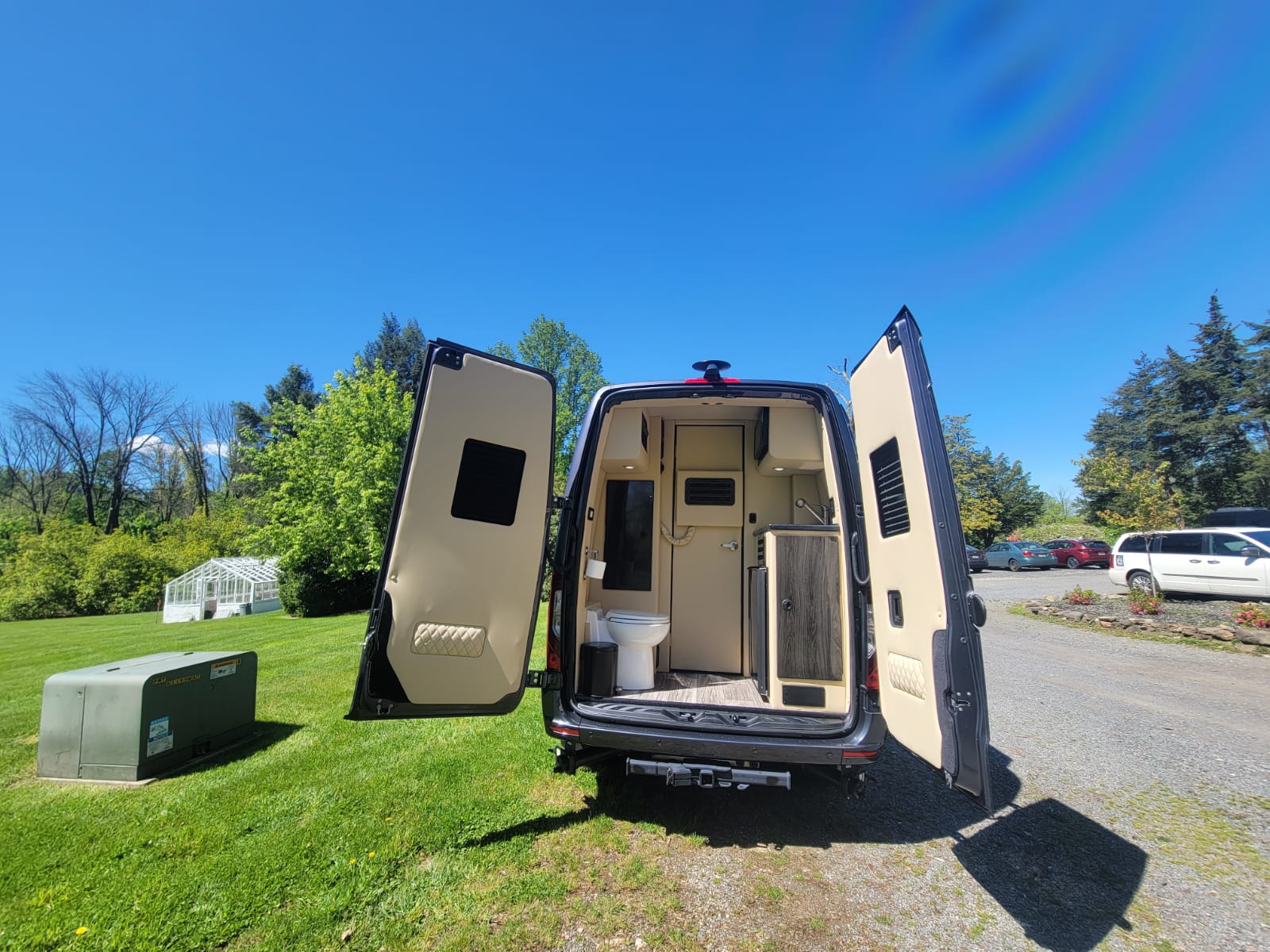 parked amidst trees & houses on a sunny day.|Open side door of a custom luxury RV rental