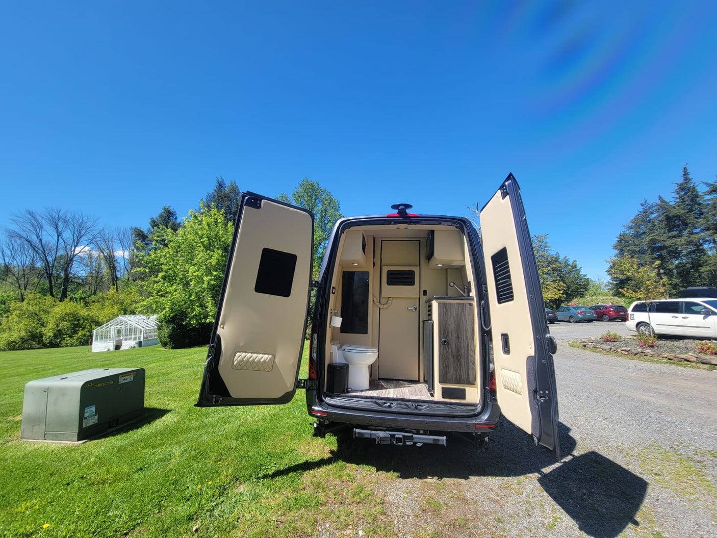 parked amidst trees & houses on a sunny day.|Open side door of a custom luxury RV rental