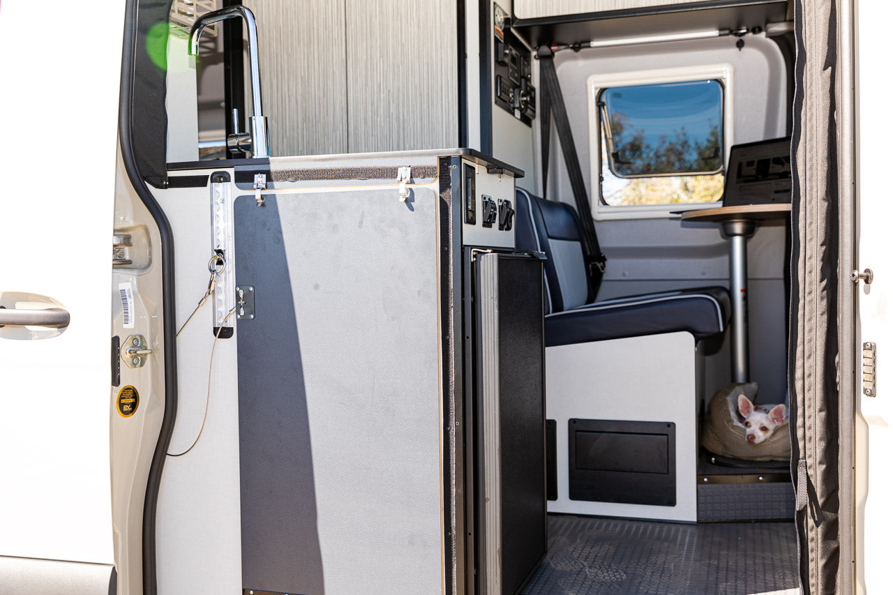 RV rental interior with a functional kitchenette, control panel, seating, and a small dog in a cozy bed. Your mobile home!